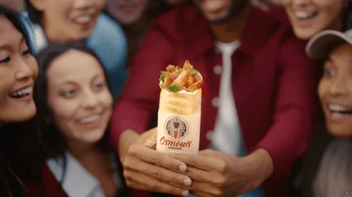 A group of friends excitedly holding a wrapped food item.