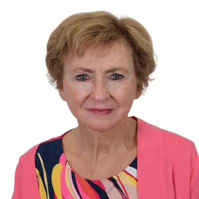 A woman in a colorful blouse and pink cardigan smiling.