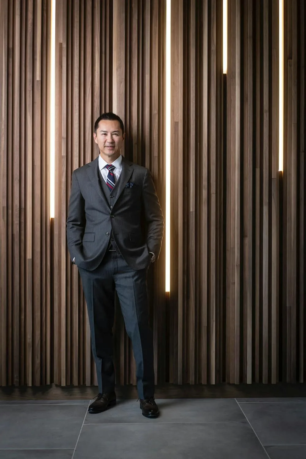A man in a suit standing by a wooden wall.
