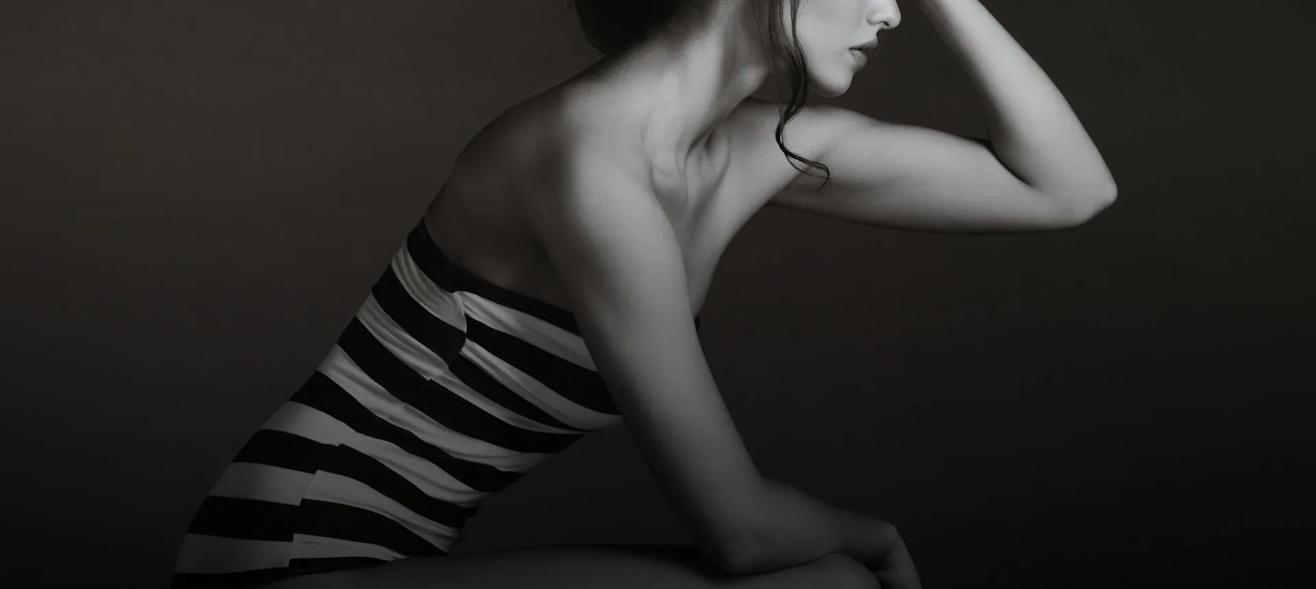 A woman in a striped swimsuit posing gracefully in profile.