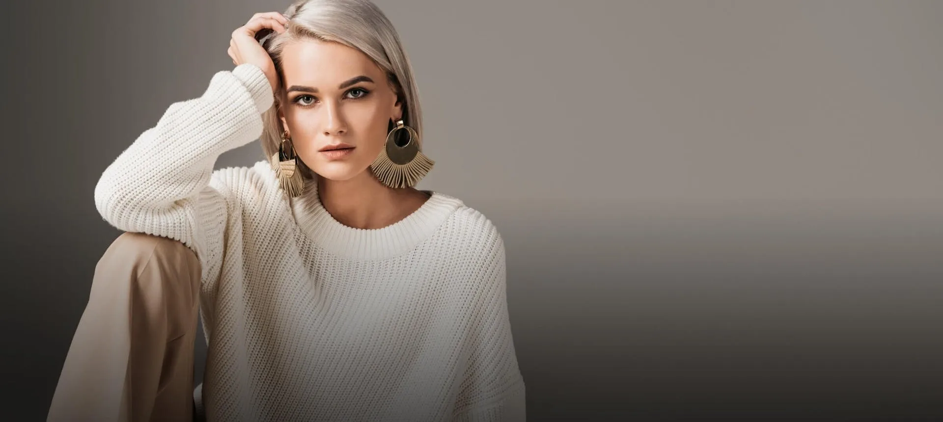 A young woman in a white sweater sits against a neutral backdrop.