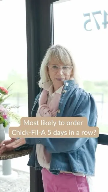A woman in a denim jacket poses indoors with flowers.