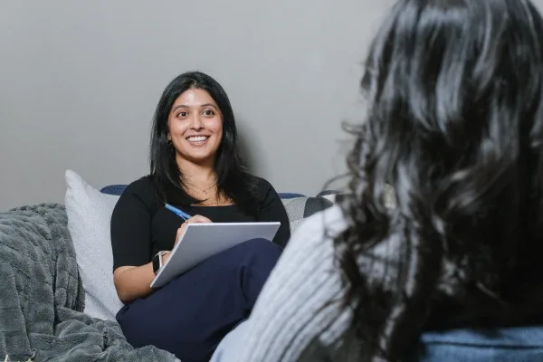 A woman smiling while taking notes in a comfortable setting.