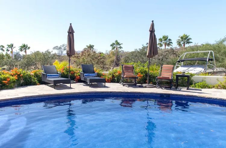 A swimming pool area with lounge chairs and tropical plants.