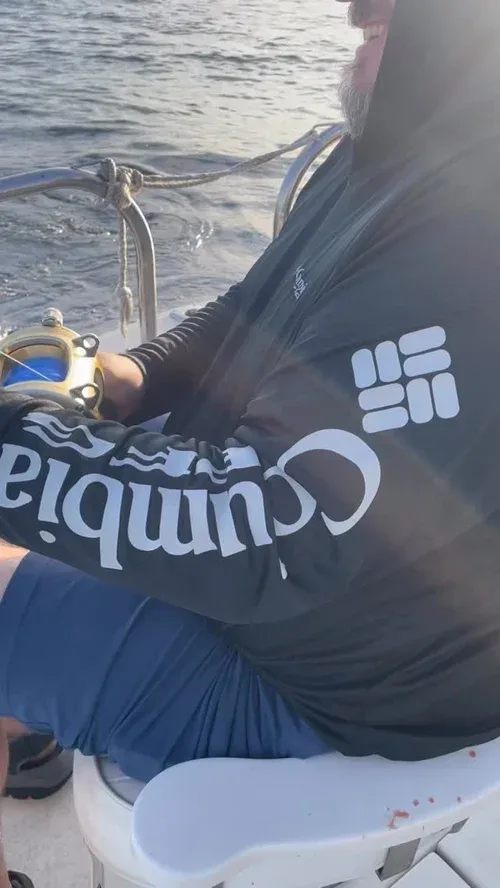 A man on a fishing boat wearing a hoodie and shorts.
