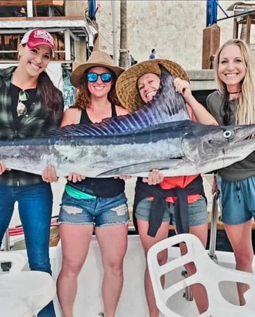 Four women holding a large marlin on a boat.