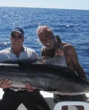 Two fishermen holding a large marlin on a boat.