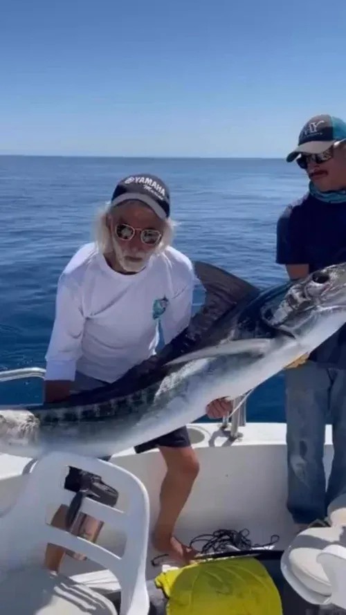 Two fishermen holding a large marlin on a boat.