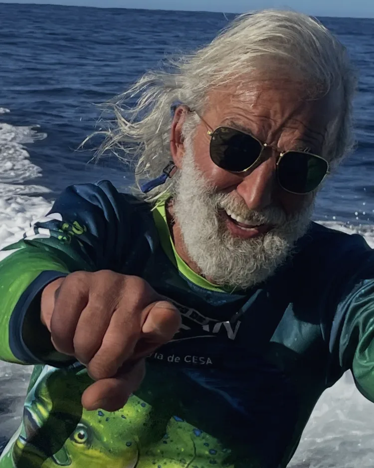 An older man with gray hair pointing at the camera on a boat.