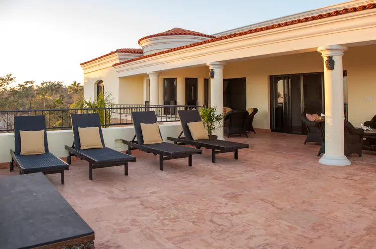 An outdoor terrace with black lounge chairs and a sunlit view.