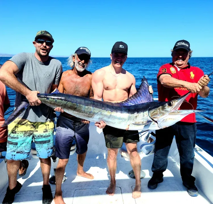 Four men holding a large marlin on a fishing boat.