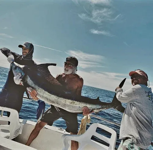 Three men holding a large marlin on a boat.