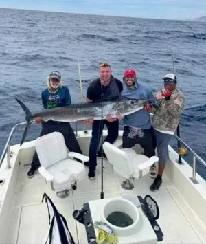 Four men on a boat holding a large fish.