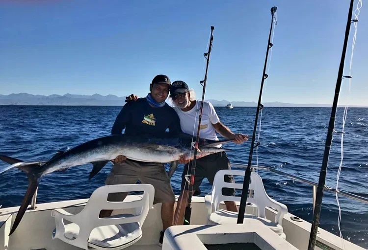 Two anglers holding a marlin on a fishing boat.