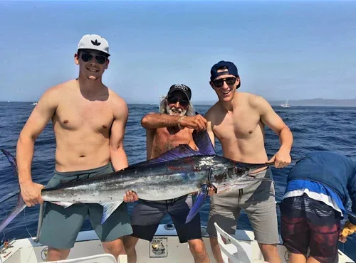 Three men smiling on a boat with a marlin caught.