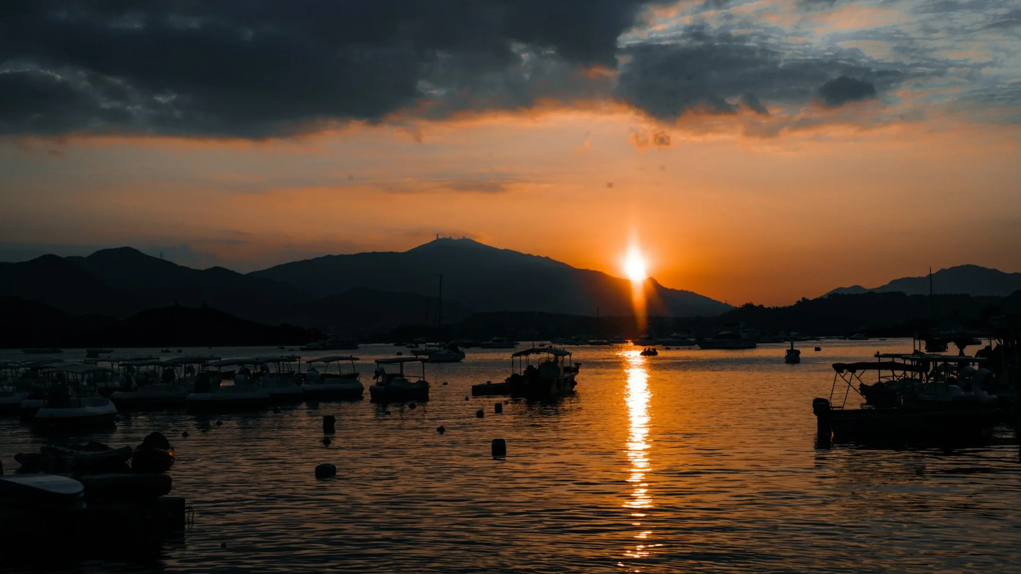 Sunset over a harbor with boats and mountains in the background.