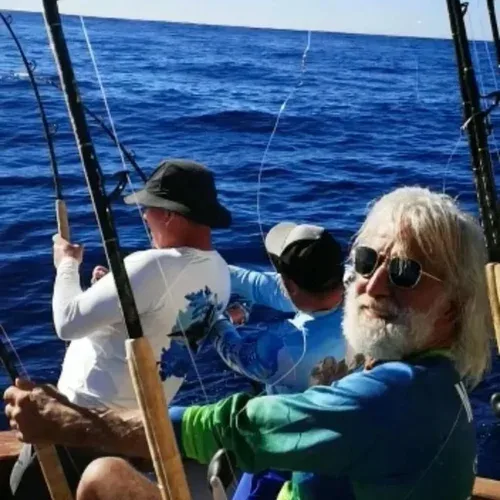Three fishermen on a boat casting fishing lines into the ocean.