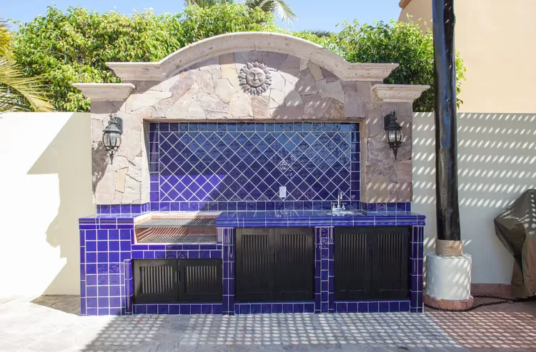 Outdoor kitchen with blue tiled countertop and grill.