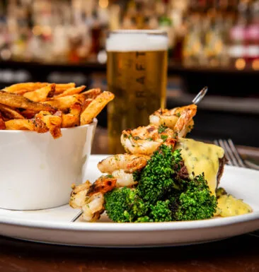 Surf and turf dish with shrimp, steak, broccoli, and fries.
