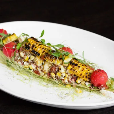 Grilled corn with watermelon and microgreens on a white plate.