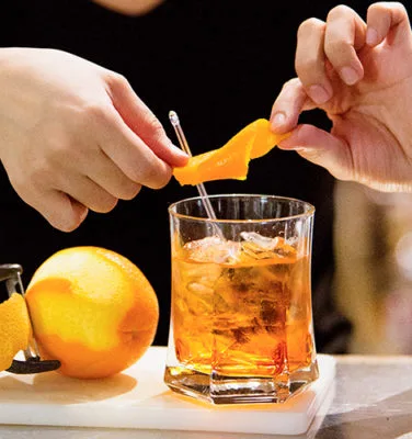 A bartender garnishing a drink with orange peel.