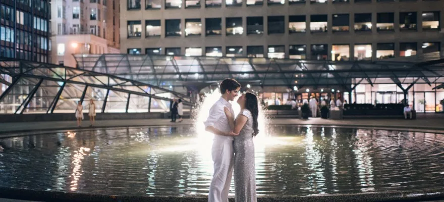 Couple by a fountain in an urban setting at night.