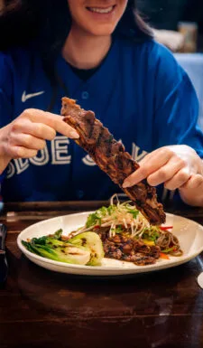 A person holding grilled meat over a plate of vegetables.