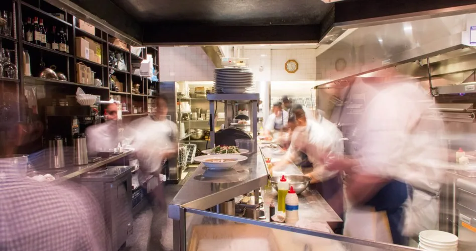 A busy kitchen with chefs preparing food and shelves of ingredients.