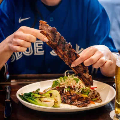 A person holds grilled meat over a plate of food.