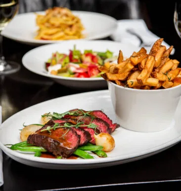Plate of steak frites with fries and salad in background.