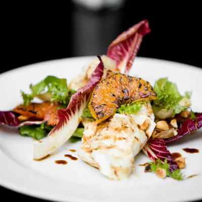 Grilled fish dish with mixed greens and orange garnish