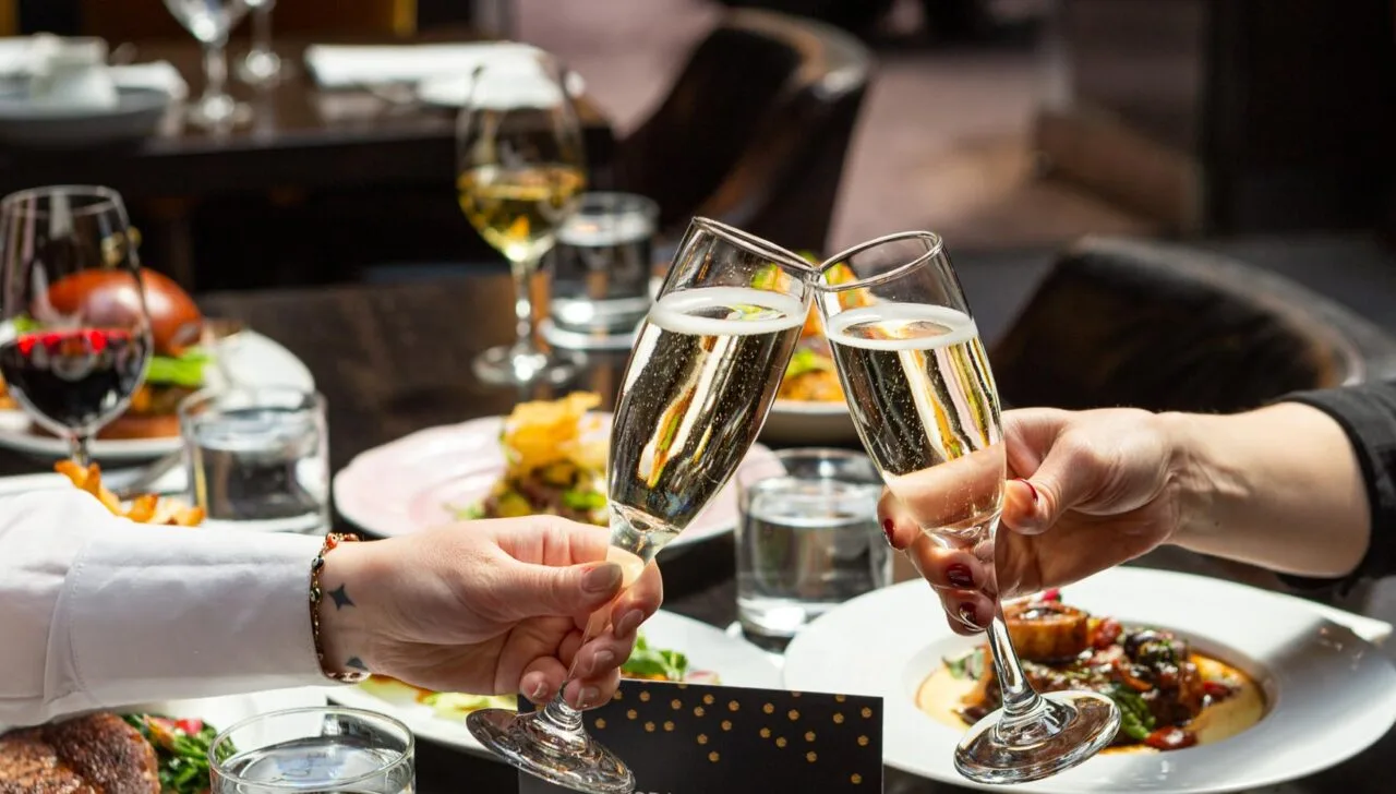 Two hands toasting with champagne flutes at a restaurant table.