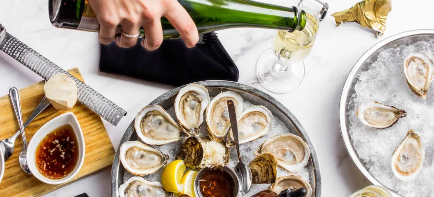 A hand pouring champagne next to a platter of oysters.