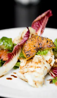 A colorful salad with grilled fish and orange slices.