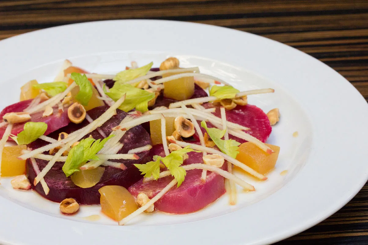 A colorful salad with beets, apples, and hazelnuts on a white plate.