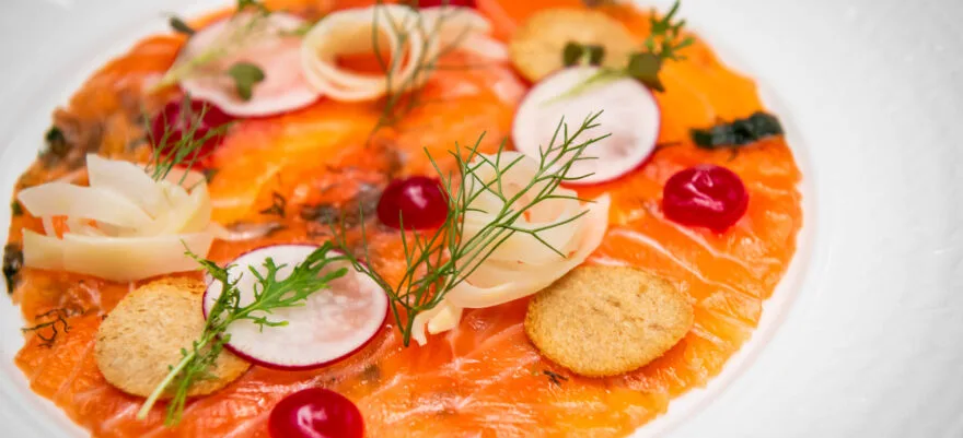 A plate of salmon gravlax garnished with herbs and radish slices.