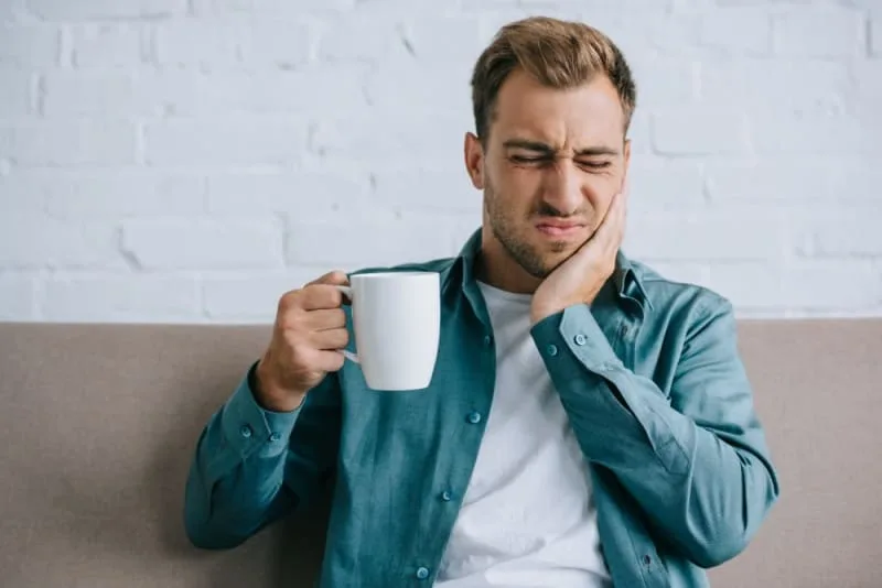 A man grimacing in pain while holding a coffee mug.