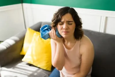 Woman holding an ice pack to her cheek in pain.