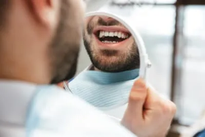 Man smiling at his reflection in a mirror at a dental office.