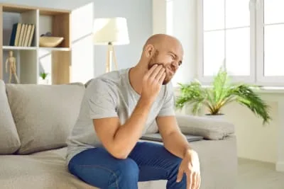 A man experiencing dental pain seated on a couch.