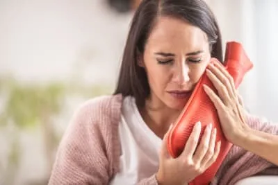 A woman holding a hot water bottle to her face.