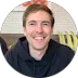 A smiling man in a black hoodie at a table.