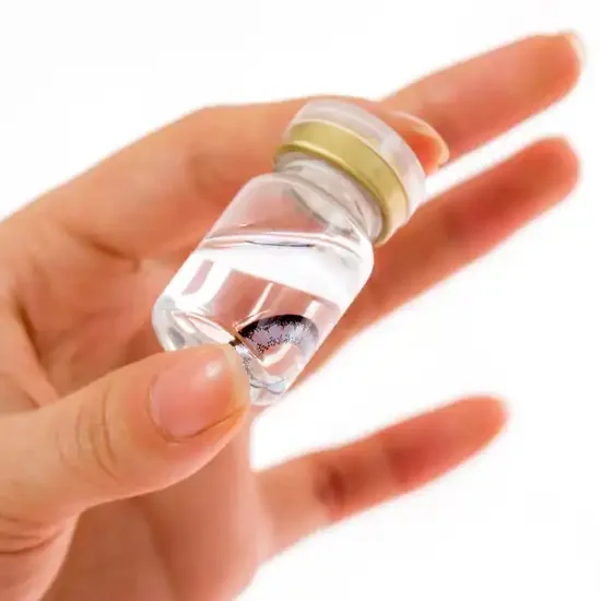 A hand holding a vial of scleral contact lenses.