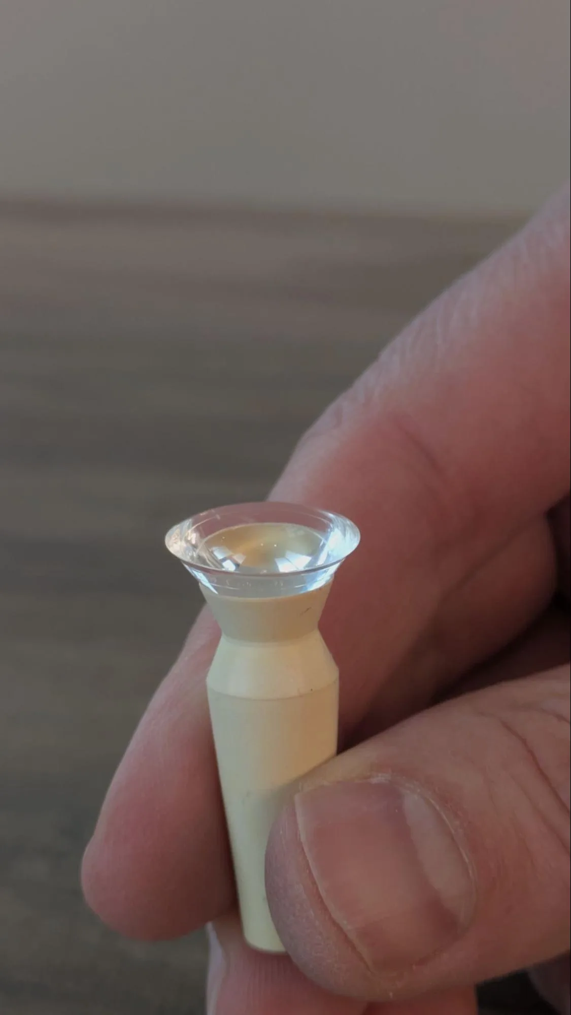 A hand holding a scleral contact lens on an insertion tool.