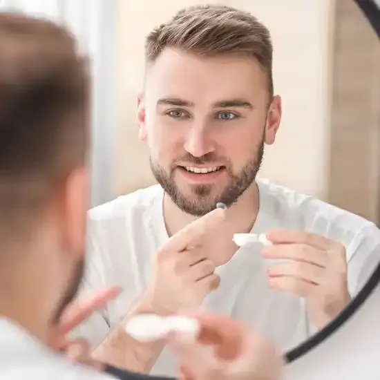 A man applying contact lenses in front of a mirror.