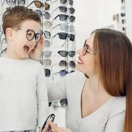 A woman assists a boy with eyeglasses in an optometry clinic.