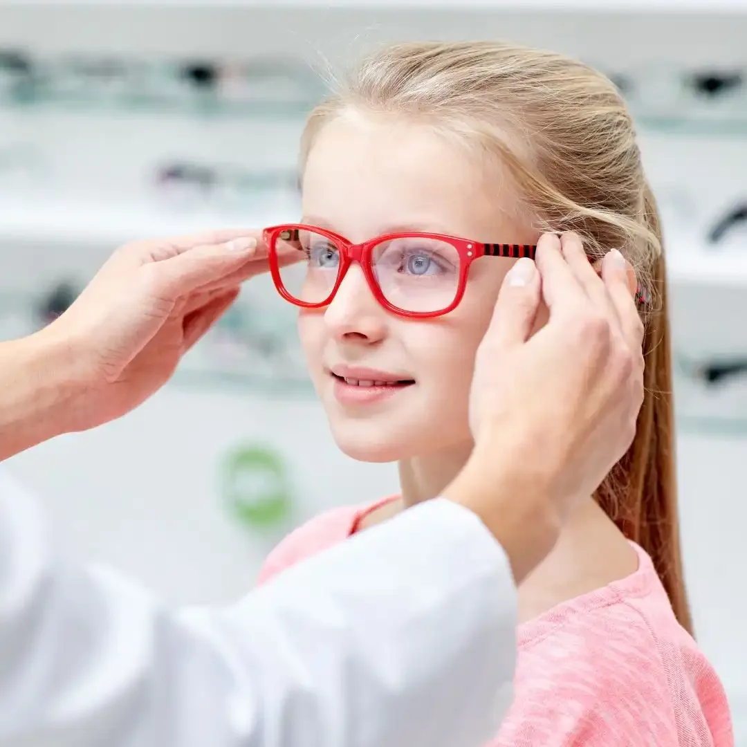 A girl being fitted with red glasses in an optometry clinic.