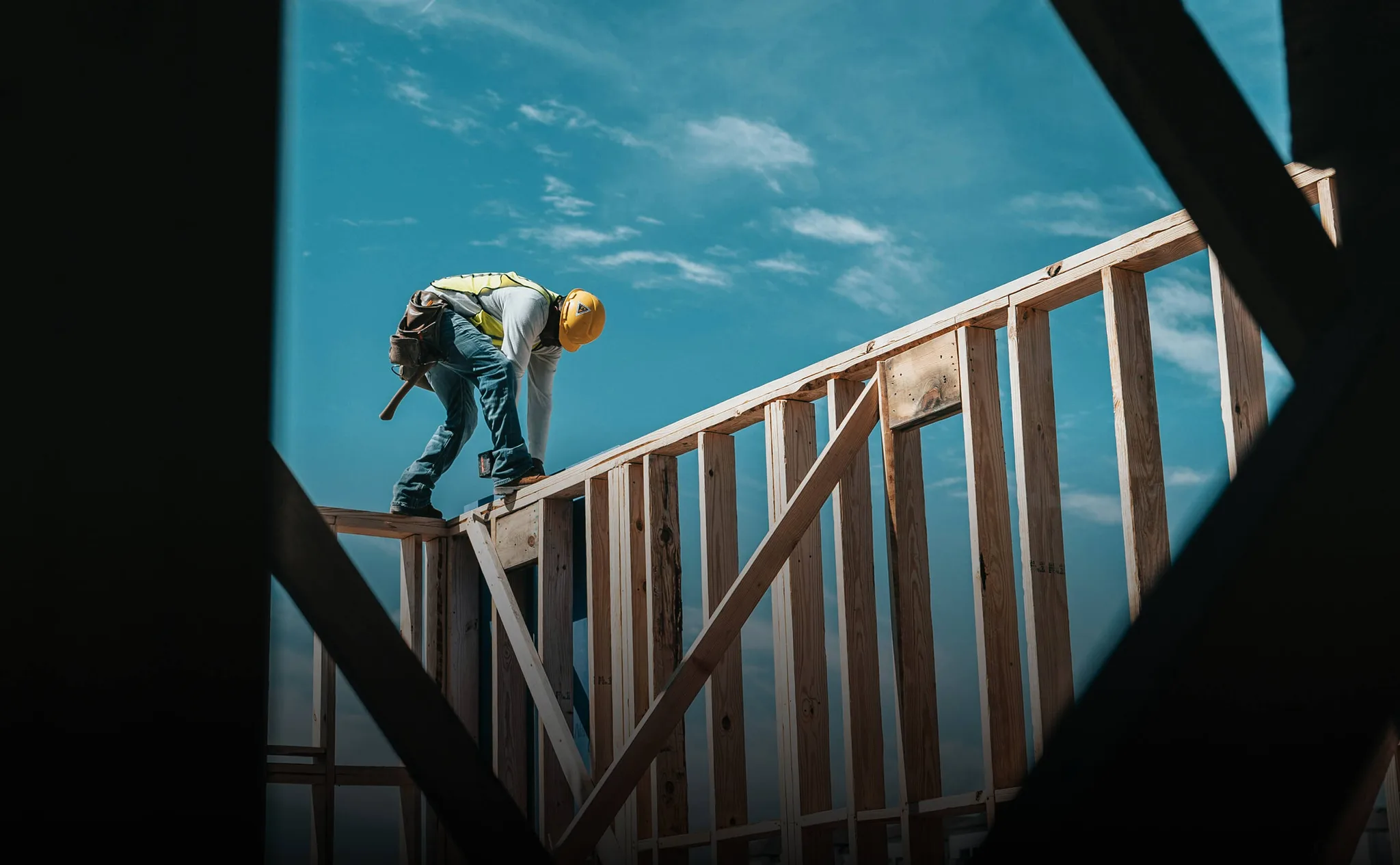 Construction worker on a wooden beam against a blue sky.