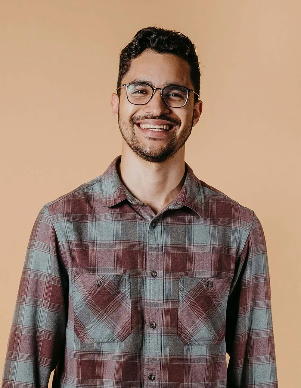 A smiling man in a plaid shirt with glasses.