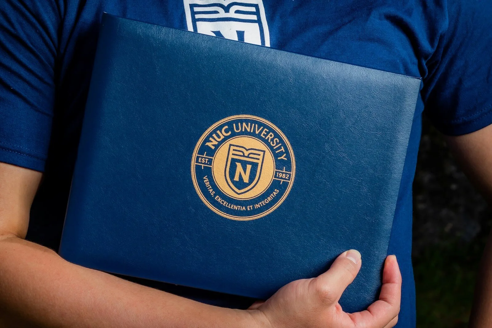 A person holding a blue folder with NUC University emblem.